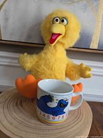 Big Bird plush seated with Cookie Monster mug front view