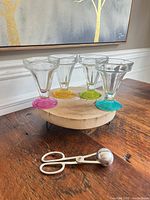Group shot of four coloured-base sundae glasses on wood riser with metal ice cream scoop in foreground