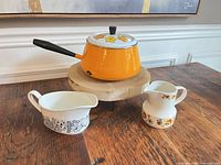 saucepan with lid and two creamers on wooden surface
