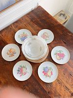 Top view showing six plates with fruit designs surrounding stacked bowls