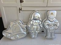 Front view of all three Wilton aluminum cake pans: bells, girl, soldier