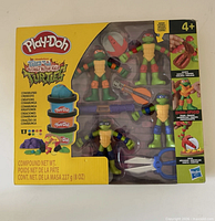 Front of sealed Play-Doh Teenage Mutant Ninja Turtles Cowabunga Creations Set box showing included figures, accessories, compound cans, age rating 4+
