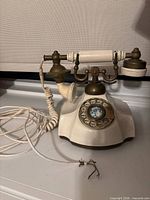 Front view of cream and brass-tone Contessa Regal rotary phone showing handset, body, rotary dial and damaged external line