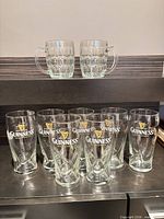 Front view of two glass beer steins and seven Guinness pint glasses