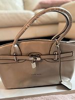 Front view of beige Caide Deor handbag showing shape, lock, handles