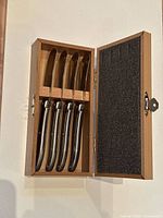 Open wooden box displaying four stainless steel Laguiole cheese knives