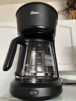 Front view of Oster drip coffee maker showing carafe measurement markings and power button