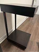 Full view of wooden side table showing top, support column, lower shelf and casters