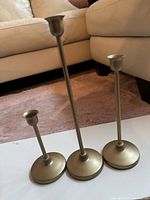 Three slim gold-tone metal candle holders grouped, showing height differences and bases