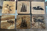 Top view of six square stone coasters displaying graphics