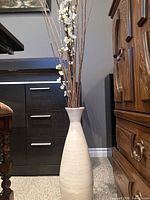 Full view of vase with twigs standing against furniture