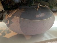 Side view of low oval ceramic vase showing white and blue speckled glaze and cream band