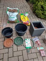 Group shot of soil bags, black pots, grey wicker planter, saucers, topiary support, pot feet
