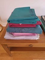 Stack of folded green, burgundy, teal and pink tablecloths on table