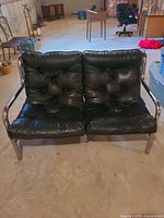 Front view of black faux leather two-seat sofa showing tufted cushions and chrome arms