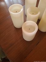 Six ivory wax flameless pillar candles grouped on table, showing height variations