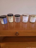 Five assorted glass-jar candles arranged on wood surface