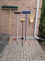 Five cleaning tools lined against brick wall