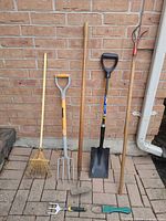 Full view of six long-handled and two hand tools against brick wall