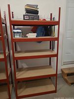 Front view of single shelving unit showing red frame and five chipboard shelves