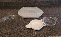 All components laid out: glass pie dish, steamer base with tray and lid, egg cooker base and lid