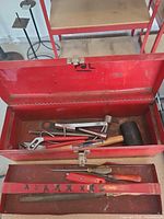 open red metal toolbox showing hand tools inside and beneath