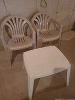 Two off-white resin patio chairs beside one square resin side table