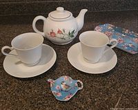 Full set arranged on countertop: teapot, two cups on saucers, tray, teabag rest
