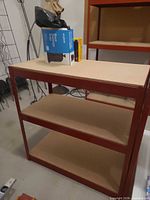 Front view of shelving unit showing red steel frame and three particle board shelves