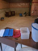 all five plastic items on table: cereal dispenser, rectangular container with red lid, and three blue ice cube trays