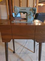 Singer teal sewing machine installed in wood cabinet