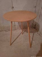 round three-leg wooden side table against concrete wall