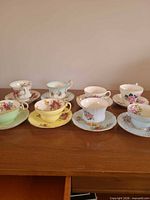 All 8 teacup and saucer pairs on wooden surface