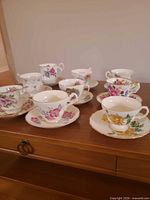 Group of nine teacup and saucer pairs on wooden table