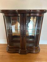Front view of wood curio cabinet showing glass doors, interior glass shelf and curved base