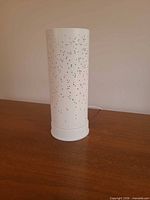Full view of white cylindrical perforated table lamp on wooden surface