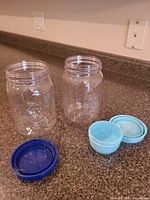 Both clear plastic jars with lids removed showing interiors and separate lids (navy blue, light blue)