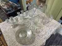 Full lot on lace cloth showing pitchers, jar, candlesticks, plates, bowls, heart dish