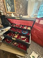 Open jewelry box showing red velvet interior and assorted costume jewelry in trays