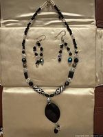 Full view of necklace laid flat with earrings above