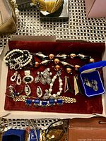 Overview of jewelry pieces arranged in red velvet tray including necklaces, bracelets, earrings and cufflinks in blue box