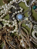 Overview of assorted pearl, chain and cabochon necklaces on green surface