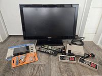 Front view of RCA TV, remotes, mini console, controllers, packaged speakers and cable