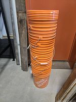 Stack of nine orange 5-gallon Home Depot buckets with handles
