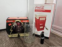 All four Coca-Cola items together: mini fridge box, ornament box, glass, mini bottle
