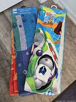 All three folded beach towels, Toy Story towel on top showing Buzz Lightyear, partial views of red-yellow and blue-purple towels underneath