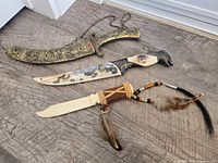All three items laid out: curved knife with scabbard, wolf-head knife, leather-wrapped letter opener