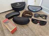 All items laid out: multiple cases, two visible sunglasses, braided belt, small red box