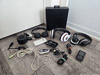 Group shot of all items on floor including speaker, headphones, MP3 players, power banks, case and cables