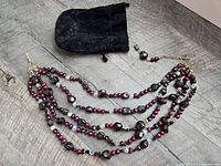 Full view of six-strand garnet and glass bead necklace with velvet pouch